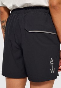 Svarta sportshorts med en strukturerad väv, elastisk midja, en liten sidoficka och en reflexgrå logotyp "ATW" på den nedre delen av benet.