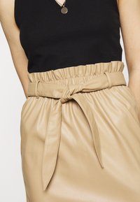 Beige fusk läderkjol med en knutdetalj i midjan och elastisk midja, parat med en svart ribbad linne.