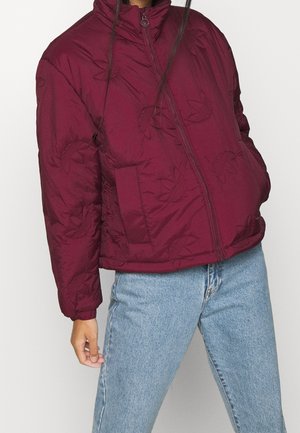 Giacca imbottita bordeaux con collo alto, caratterizzata da un motivo floreale in rilievo, chiusura con zip e tasche laterali, abbinata a jeans azzurri.