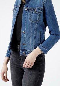 Jeansowa kurtka w średnim niebieskim kolorze o dopasowanym kroju, z dwiema kieszeniami na piersiach, miedzianymi guzikami i lekko przetartym wykończeniem.