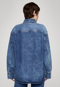 Oversizowa kurtka dżinsowa w jasnoniebieskim kolorze z efektowną, wypraną teksturą, widocznymi szwami i mankietami zapinanymi na guziki. Posiada klasyczny kołnierz i prosty krój.
