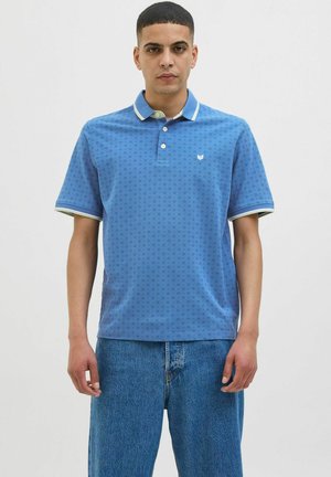 Kortærmet blå polo skjorte med diamantmønster, to-knap lukning og kontrasterende krave. Sammen med lyseblå lige ben jeans.
