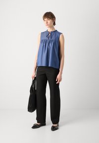 Μπλε αμάνικο τοπ με ρυάκωτη λαιμόκοψη, χαλαρή εφαρμογή, συνδυασμένο με μαύρες φαρδιές παντελόνες και μαύρες λαστιχένιες γόβες, κρατώντας μια μαύρη τσάντα.