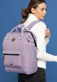 Sac à dos violet clair en tissu, avec une poche zippée à l'avant, des poignées supérieures et des bretelles rembourrées ajustables.