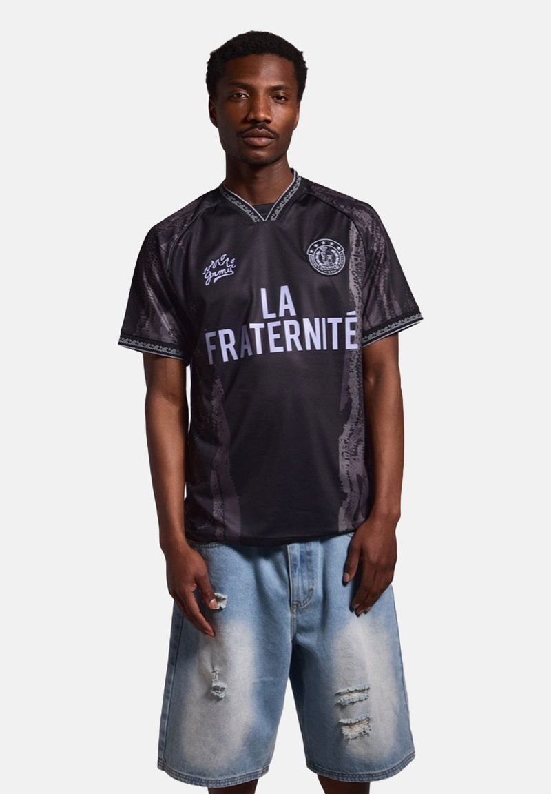 Jersey negro con "LA FRATERNITE" en azul claro. Presenta un cuello en V, patrones contrastantes y mangas cortas. Combinado con pantalones cortos ligeros deslavados en azul claro.