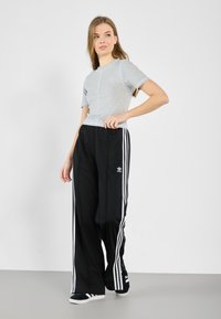 Grå tettsittende T-skjorte med korte ermer og kontrastsøm, kombinert med svarte joggebukser som har hvite sidestreker og logo. Svarte joggesko.