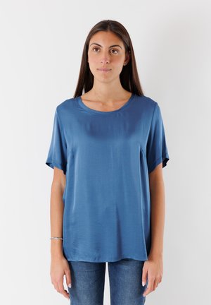 Top blu in satin a maniche corte con scollo rotondo, vestibilità ampia e texture liscia, abbinato a jeans scuri. Nessun motivo o accentuazione visibile.
