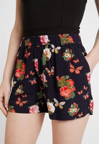 Kwiatowe szorty z ciemnoniebieskim tłem, elastycznym pasem i żywymi czerwonymi, różowymi oraz zielonymi wzorami kwiatów i motyli.