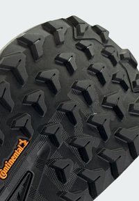 Suela de zapato de caucho negro con un patrón de banda de rodadura agresivo de tacos triangulares, que presenta una superficie texturizada y un pequeño logotipo naranja "Continental".