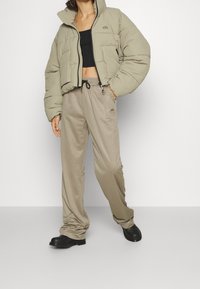 Puffer jacket in light khaki, cropped design, featuring two front pockets. Matching beige sweatpants with drawstring waist, loose fit, and logo detail.