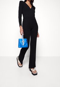 Body nero a maniche lunghe con pantaloni neri a coste, abbinati a una borsa blu con una tracolla decorata con strass e ciabatte oversize.
