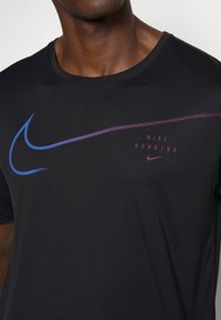 Svart träningsskjorta med blå och lila Nike-logotyp samt texten "NIKE RUNNING". Slät, fukttransporterande tyg med korta ärmar.