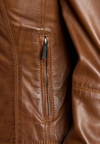 Suure plaani pruun nahkjakki tasku, millel on vertikaalne lukk ja tekstuuriga õmblused siledal nahapinnal.