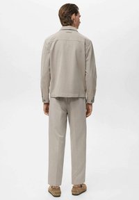 Veste beige légère à coupe droite et avec des poignets boutonnés, assortie à un pantalon tailleur, vue de dos.