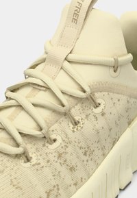 Μπεζ αθλητικά παπούτσια με υφασμάτινη επιφάνεια και στίγματα. Διαθέτουν επίπεδους κορδόνια, κυκλικές θυρίδες και χοντρή σόλα. Λουράκι για εύκολη χρήση.