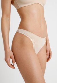 Bas de bikini couleur chair en tissu lisse et extensible. Présente un design minimaliste avec des côtés fins et une coupe médiane à l'arrière.