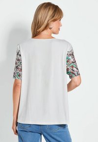 Witte T-shirt met kleurrijke, patroonachtige korte mouwen, voorzien van ingewikkelde bloemmotieven. Zachte stof, relaxed fit en ronde halslijn.