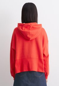 Rode cropped hoodie met een voorzak en een capuchon met trekkoord. Zacht materiaal met geribbelde manchetten en zoom, van achteraf getoond.