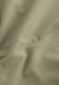 Tissu beige lisse avec des plis doux et une texture subtile visible sous un éclairage doux.