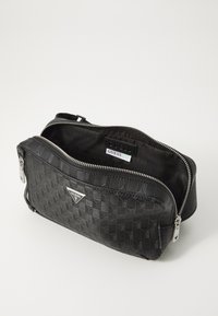 Black zippered handbag made of textured material, featuring a diamond pattern and silver-tone hardware; includes brand logo on the front.