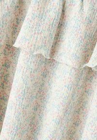Tessuto morbido con piccoli motivi floreali rosa e blu su sfondo bianco, caratterizzato da un bordo ondulato.