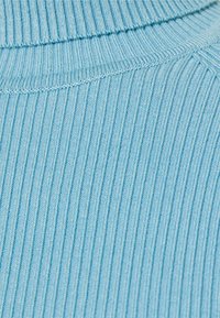 Jasnoniebieska żebrowana tkanina z wysokim kołnierzem. Tekstura jest miękka, z wyraźnymi pionowymi paskami i starannymi detalami szycia.