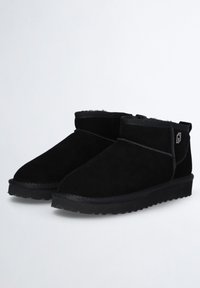 Botines de ante negro con suela de goma plana, que cuentan con un cuello corto, costuras mínimas y un pequeño logotipo en el lateral.