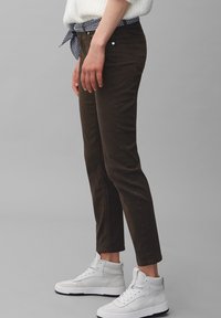 Pantaloni slim-fit marroni, realizzati in tessuto morbido, con vita media, tasche laterali e abbinati a sneakers alte bianche.