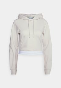 Zkrácená mikina v světle béžovém materiálu s kapucí na šňůrku, dlouhými rukávy a bílým elastickým pasem s logem Calvin Klein.