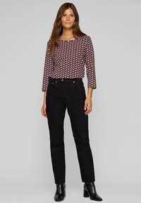 Schwarze Denim-Hose mit geradem Bein, kombiniert mit einem roten und weißen Langarmoberteil mit geometrischem Muster. Das Oberteil hat einen runden Ausschnitt und einen lässigen Schnitt.