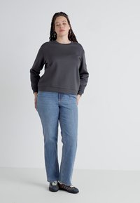 Grå genser med rund hals laget av mykt stoff, kombinert med lys blå jeans med rett ben. Modellen står med hendene i lommene iført sneakers.