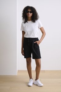 Shorts noirs en coton avec poches latérales, taille élastique et poignets retroussés, associés à un t-shirt blanc ajusté et des baskets blanches.