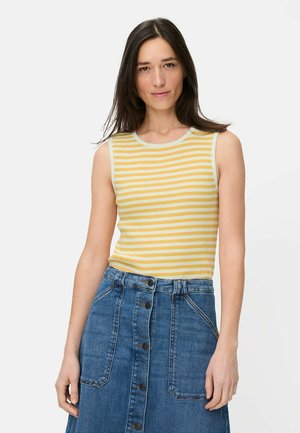 Kvinde med langt mørkt hår iført en ærmeløs gul og hvid stribet top, der er stoppet ned i en blå cowboynederdel med højtaljet front med knapper.