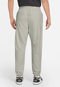 Un pantalon de jogging gris clair avec une taille élastique, des poches latérales et une coupe décontractée, associé à des baskets noires sur un fond neutre.