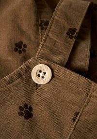 Pruun sametkangas mustade käpajälje mustritega, millel on suur ümmargune puidust nupp lillelise väljalõikega.