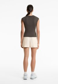 Bruine aansluitende mouwloze top met een ronde hals, gedragen met lichte shorts en witte sneakers. Gladde textuur en minimalistisch ontwerp.