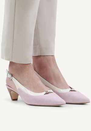 Feet wearing pale pink suede slingback heels with a low wooden heel and beige cropped pants.