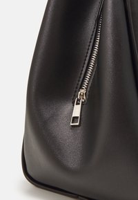 Sort læderhåndtaske med en glat overflade, en sølvlynlås med et rektangulært trækstykke og bløde, afrundede kanter.