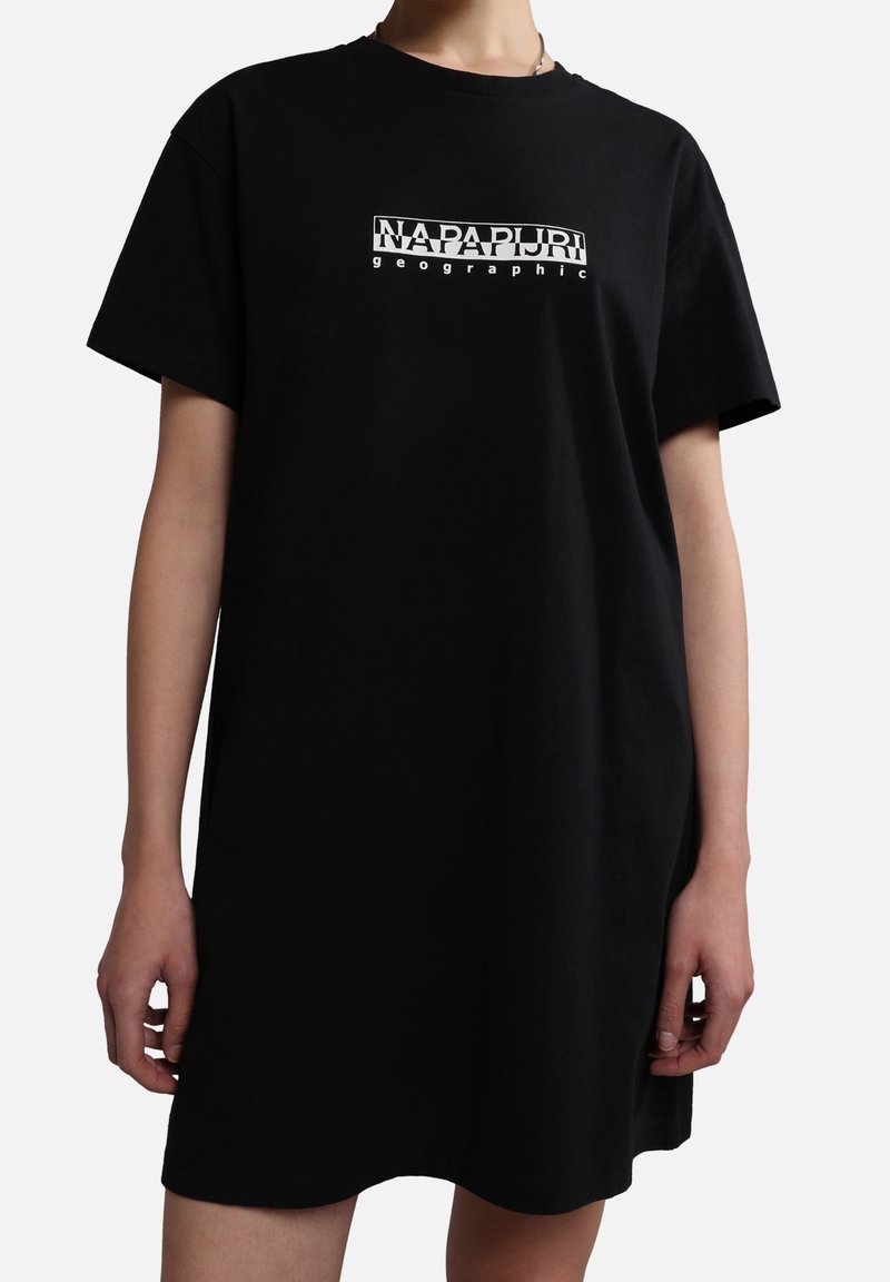 Person iført en løs sort T-shirt kjole med korte ærmer og hvid "Napapijri geographic" logo centreret på brystet.