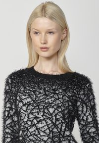 Maglione a maglia fuzzy in bianco e nero con scollatura rotonda e motivo testurizzato. Le maniche presentano una finitura morbida e piumosa.