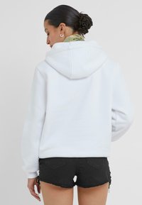 Sweatshirt à capuche blanche avec une coupe décontractée, des poignets côtelés et un intérieur doux, associé à un short en denim noir avec des bords effilochés.