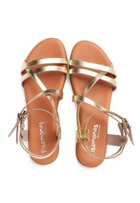 Zlaté sandále na opätku s koženou stielkou, svetlohnedou podrážkou a nastaviteľnými remienkami na členkoch. Jednoduchý a funkčný dizajn.