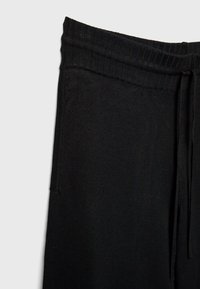 Schwarze Jogginghosen mit geripptem Bund, Zugbanddetail und weichem Stoff, die für Komfort und Bewegungsfreiheit gestaltet sind.