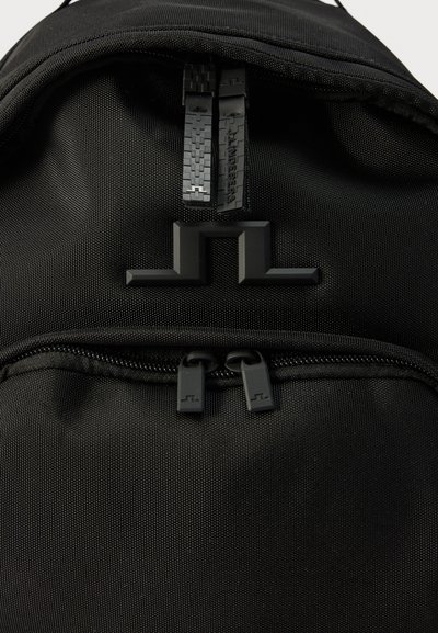 Μαύρο σακίδιο από ύφασμα με δύο φερμουάρ στην κορυφή και μπροστινή τσέπη, με ανάγλυφο γεωμετρικό λογότυπο τοποθετημένο στο κέντρο πάνω από την μπροστινή τσέπη.