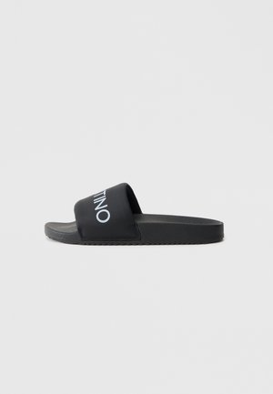 Black slide sandals with a wide strap featuring a white logo. Textured footbed and a flat rubber sole with a ridged pattern.