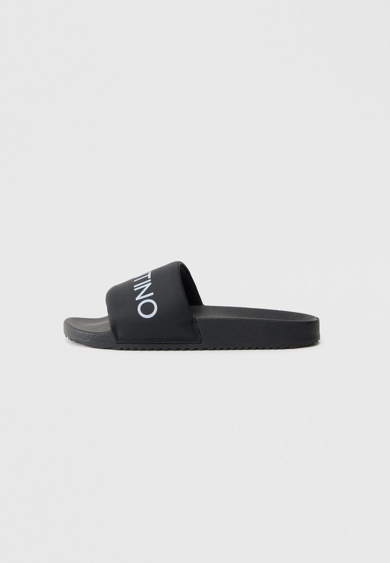 Black slide sandals with a wide strap featuring a white logo. Textured footbed and a flat rubber sole with a ridged pattern.