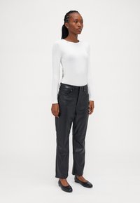 Calças de pele pretas de perna reta combinadas com uma blusa comprida branca justa; modelo em pé, com uma textura suave e design casual.