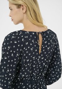 Navy floral dress with a keyhole back, featuring a soft, textured fabric and elasticated puff sleeves. Accents of white flowers throughout.