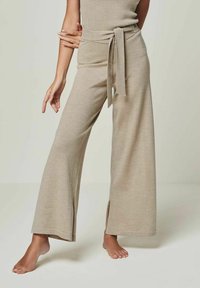 Beige wide-leg trousers made of soft knit fabric, featuring a tied waistband and side slits at the hem for added design detail.