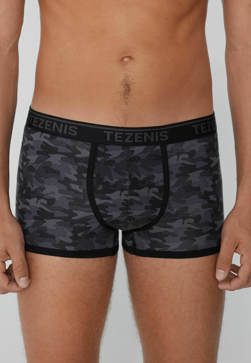 Boxers cortos de camuflaje en negro y gris con una cinturilla negra etiquetada como "TEZENIS"; fabricados con una tela suave, tienen un diseño ajustado y costuras planas.